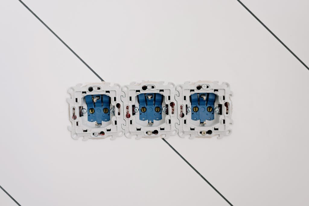 Close-up view of three blue electrical sockets installed in a white wall, showing details of wiring and connections.