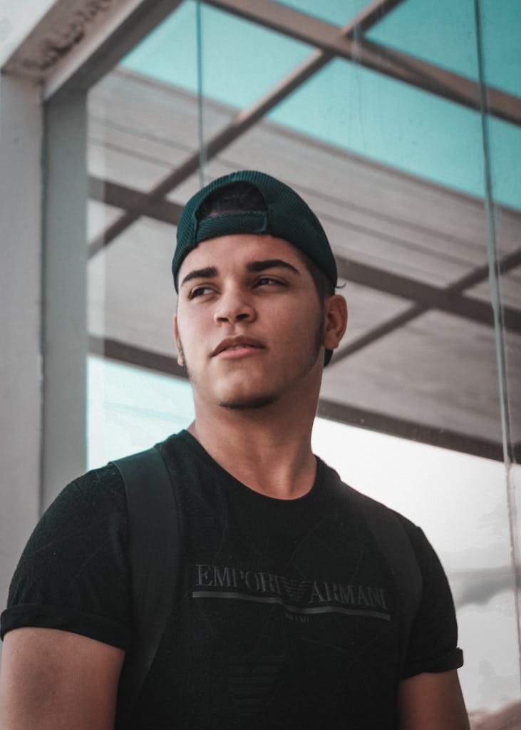 Portrait of a young man in a black shirt and cap, posing outdoors with a confident expression.