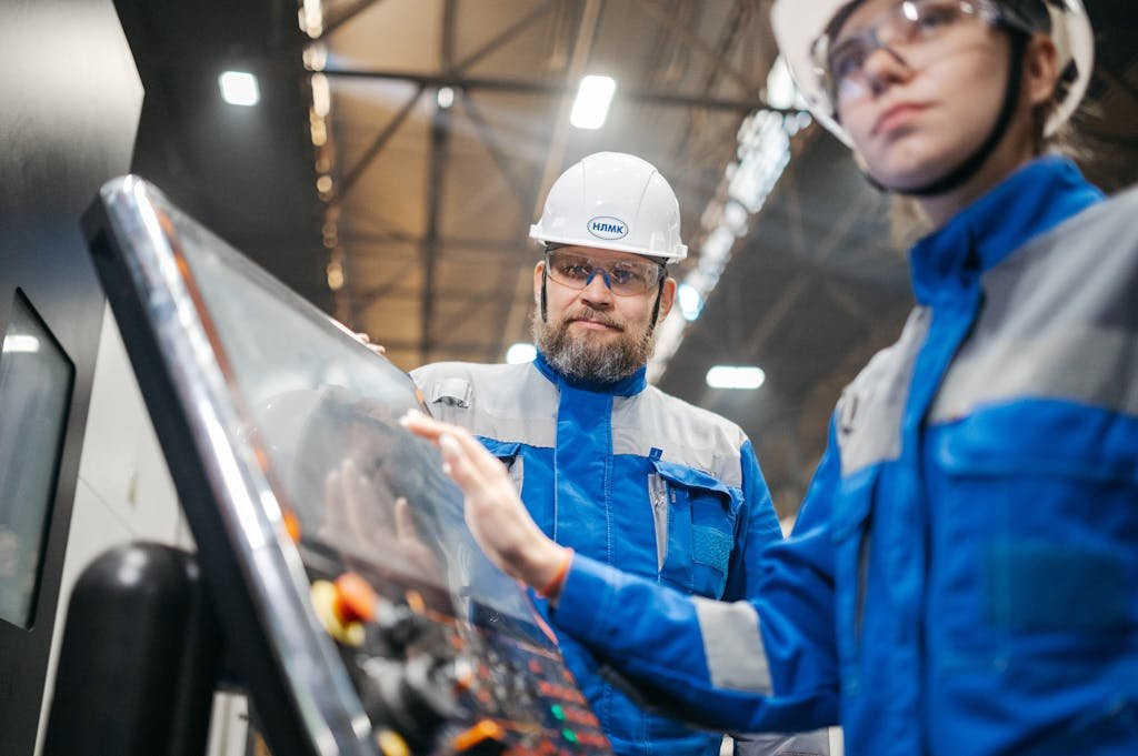 Two industrial workers in safety gear operate machinery in a modern facility.